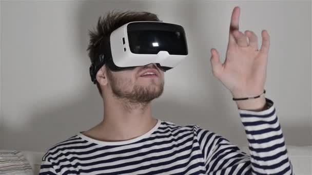 Man wearing virtual reality goggles. Studio shot, white couch - Filmati, video