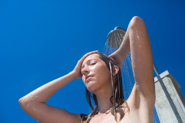 Pretty, young woman woman under shower on the beach - Foto, Imagen