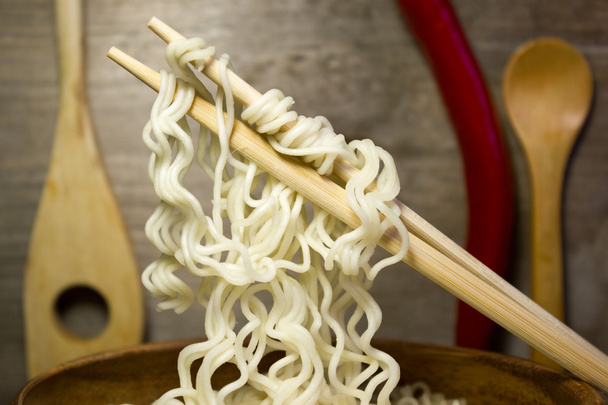 Instant noodles in a wooden bowl with chopsticks. Wooden background and red pepper. - Photo, Image