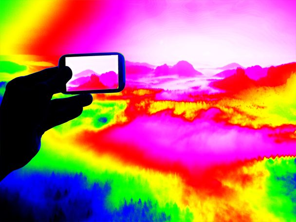 Fantastique scanner infrarouge. Main touristique prend des photos par smartphone sur le point de vue et regarder dans la vallée brumeuse de printemps
.  - Photo, image