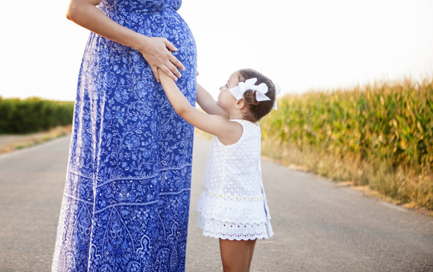 Mãe grávida e sua filha entre campos de milho
 - Foto, Imagem