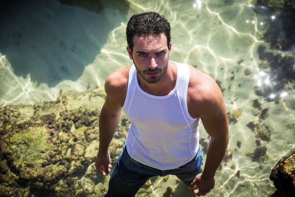 Athletic man in the sea or ocean by rocks, wet t-shirt - Photo, Image