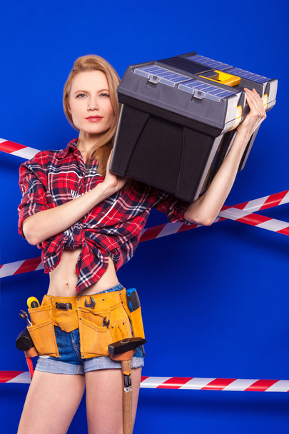Будівельник дівчина на синьому фоні з професійним будівельним інструментом в захисному шоломі
 - Фото, зображення