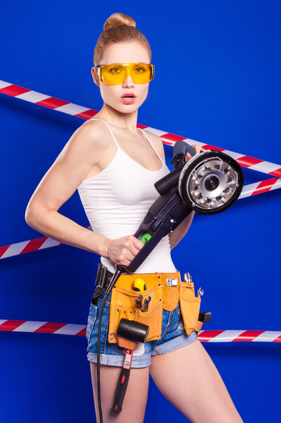 Builder girl on a blue background with a professional building tool in a protective helmet - Foto, imagen