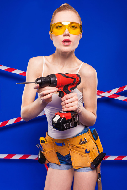 Chica constructora sobre un fondo azul con una herramienta de construcción profesional en un casco protector
 - Foto, imagen