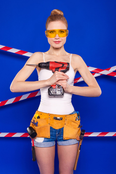 Строительница на синем фоне с профессиональным строительным инструментом в защитном шлеме
 - Фото, изображение