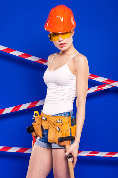 Construtor menina em um fundo azul com uma ferramenta de construção profissional em um capacete de proteção
 - Foto, Imagem