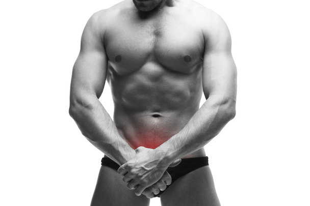 Man with pain in the prostate. Muscular male body. Handsome bodybuilder posing in studio. Isolated on white background with red dot - Photo, Image