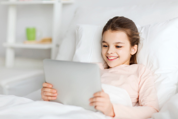 happy girl lying in bed with tablet pc at home - Фото, изображение