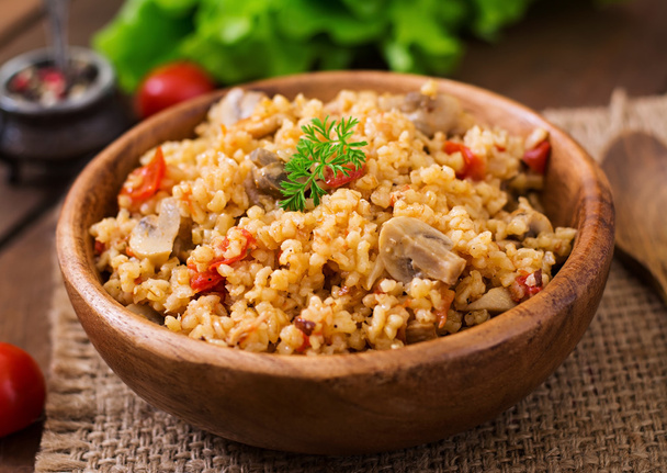 Bulgur with chicken, mushrooms and tomatoes in a wooden bowl. - Photo, Image