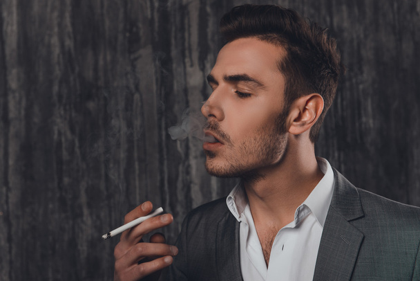 Side view of a cheeky man in suit on the grey background smoking - Фото, зображення