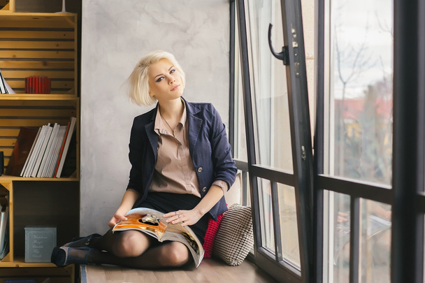 Chica sentada en el alféizar de la ventana con un diario de moda en su ha
 - Foto, Imagen