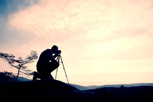 Ερασιτέχνης φωτογράφος λαμβάνει φωτογραφίες με κάμερα καθρέφτη στην κορυφή του βράχου. Τοπίο ονειρικό γεροπαράξενος, ροζ ομιχλώδη Ανατολή Άνοιξη πορτοκαλί - Φωτογραφία, εικόνα