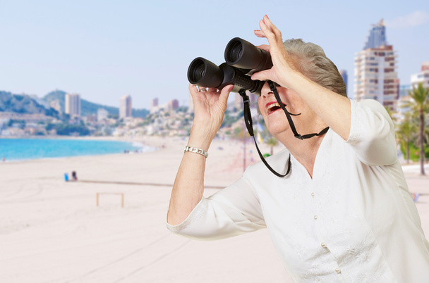 Portrait of senior woman looking through a binoculars near the b - Photo, Image