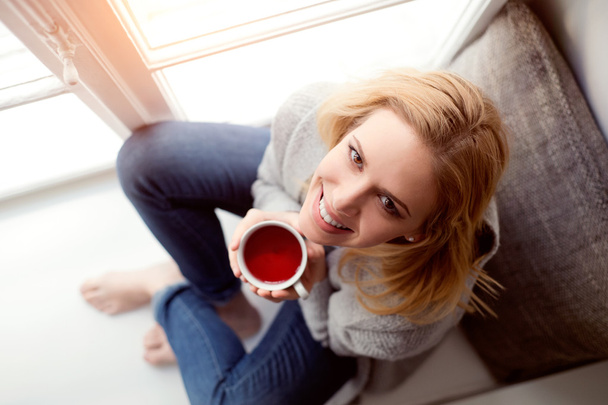 Woman on window sill with cup of tea - Фото, изображение