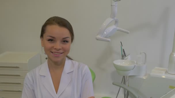 Dantist in Lab Coat is Smiling Sitting on a Green Chair at Dental Treatment Room Young Woman is Looking at Camera Panorama of a Room Hospital Ward - Filmagem, Vídeo
