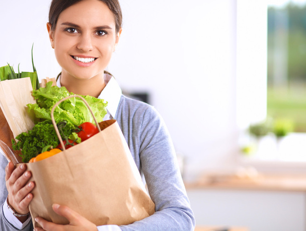 Young woman holding grocery shopping bag with vegetables .Standing in the kitchen - Foto, Imagem