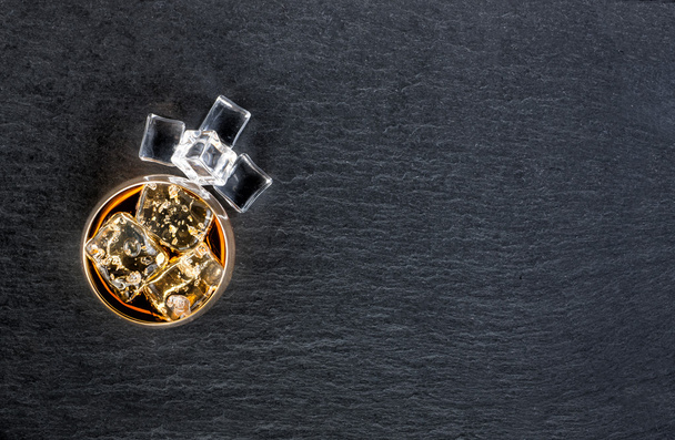 Glass of scotch whiskey and ice on black stone background - Foto, imagen