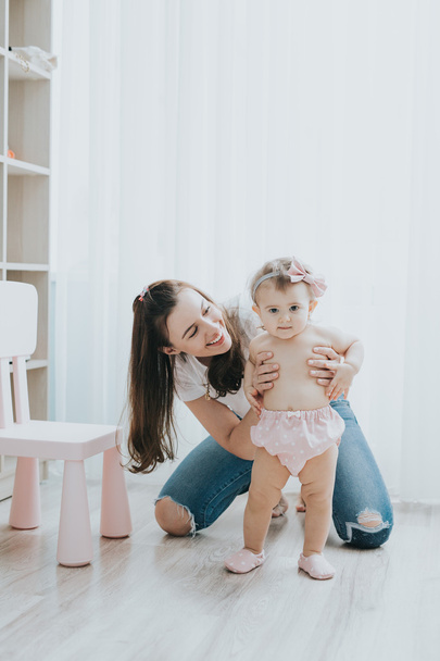 Mooie moeder portret spelen met haar schattig klein meisje in een witte ruimte in de ochtend - Foto, afbeelding