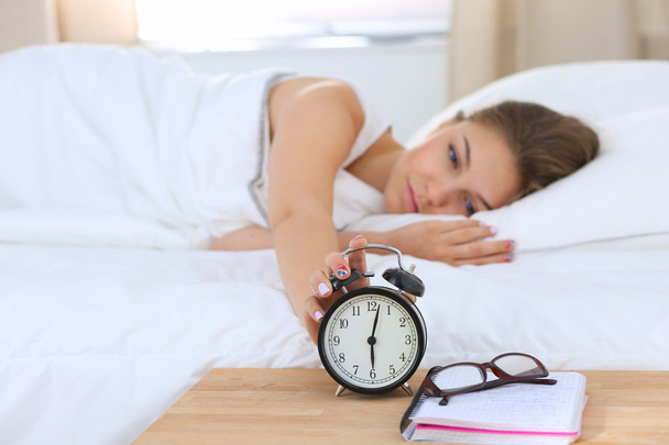 A young woman putting her alarm clock off in the morning - Foto, imagen