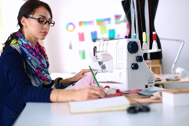 Young woman sewing while sitting at her working place - 写真・画像