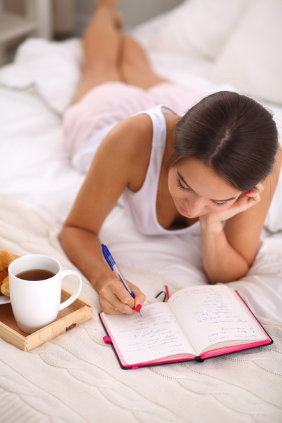 Young beautiful woman lying in bed writing a diary - 写真・画像
