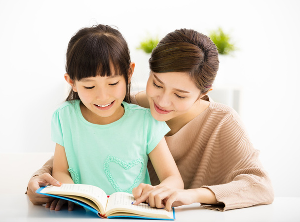 Gelukkig klein meisje op zoek naar boek met haar moeder - Foto, afbeelding