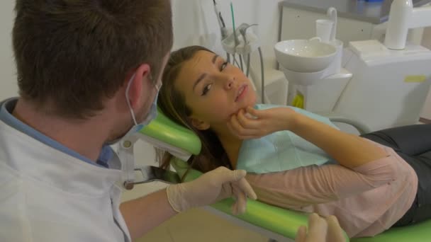 Woman is Lying on a Dentist's Chair Touches a Jaw Dentist in Mask is Talking to Patient Woman Gets up Dental Treatment Room Visit to the Dentist - Filmati, video