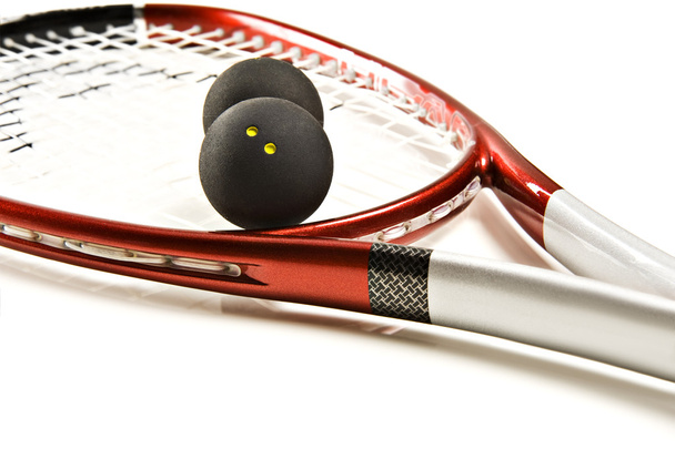 Close up van een rode en zilveren squash racket en bal op een witte achtergrond met ruimte voor tekst - Foto, afbeelding