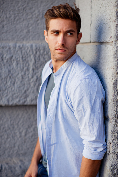 Handsome man in blue shirt standing near the wall and looking aside - Photo, Image
