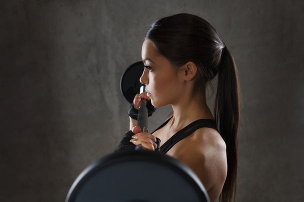 young woman flexing muscles with barbell in gym - Photo, Image