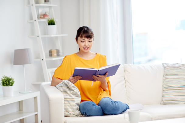 smiling young asian woman reading book at home - Φωτογραφία, εικόνα