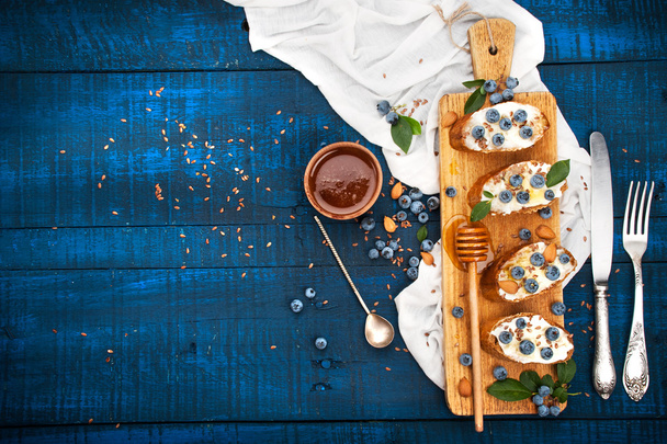 Sandwiches with soft cheese and blueberries on a wooden background. A healthy breakfast - Photo, Image