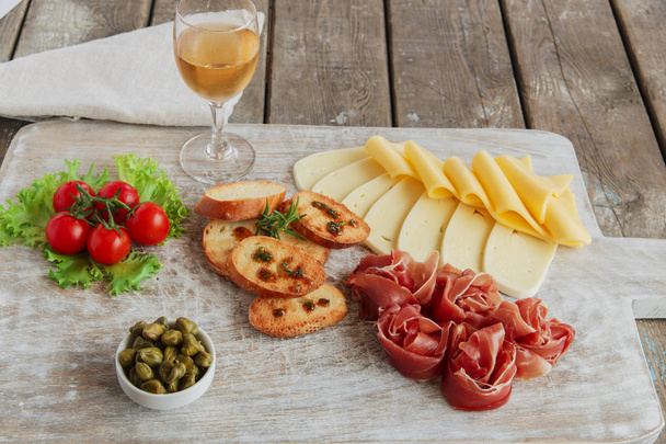 şarap - jambon, salam, peynir, Kapari, domates, lezzetli meze üzerinde hafif bir ahşap kurulunda görev yapmaktadır. - Fotoğraf, Görsel