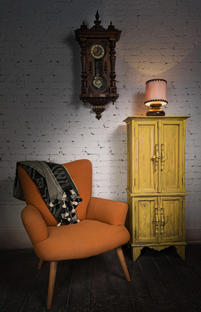 Pomarańczowy fotel, żółty szafka, wahadło zegara i oświetlony Lampa stołowa - Zdjęcie, obraz