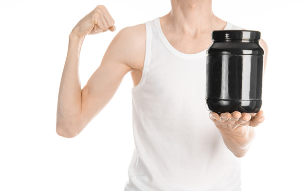 Bodybuilding and Sports theme: a thin man in a white T-shirt and jeans holding a plastic jar with a protein isolated on a white background in studio - Zdjęcie, obraz