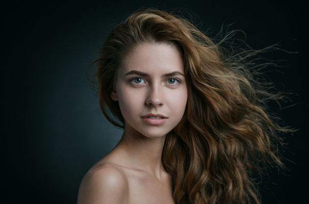 Dramatic portrait of a girl theme: portrait of a beautiful girl with flying hair in the wind against a background in studio - Photo, Image