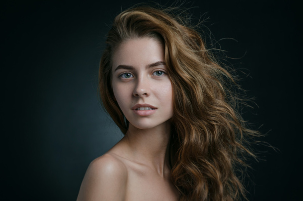 Dramatic portrait of a girl theme: portrait of a beautiful girl with flying hair in the wind against a background in studio - Fotó, kép