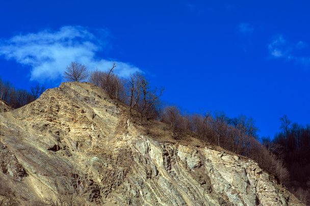 Скеля, освітлена прямим сонячним світлом на тлі блакитного неба з хмарами
 - Фото, зображення