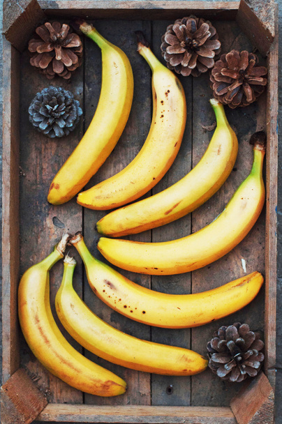 стиглі жовті банани в плетеному кошику, на дерев'яному тлі, вид
 - Фото, зображення