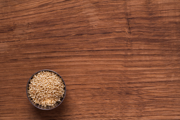 millet in metal bowl on wooden table - Foto, Imagen