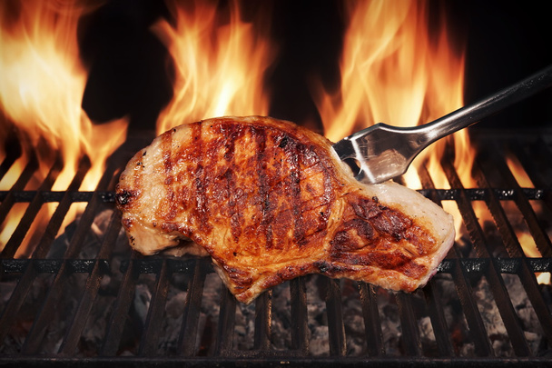 Стейк зі свинини на гарячому палаючому грилі барбекю з вилкою
 - Фото, зображення