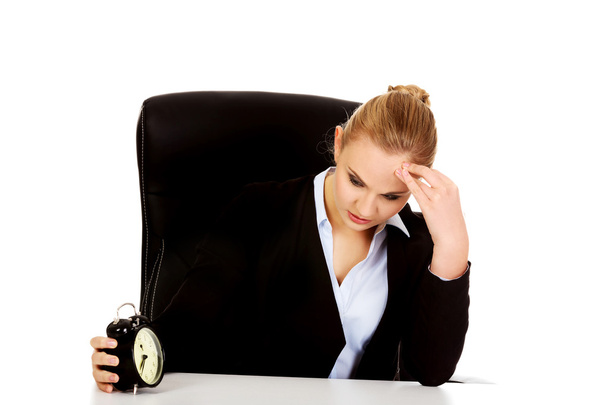 Tired business woman behind the desk with alarm clock - Zdjęcie, obraz