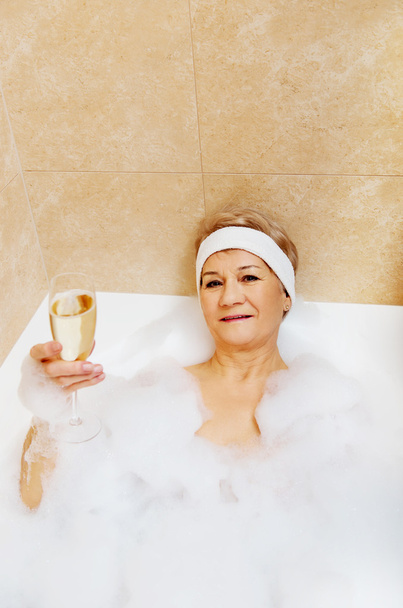 Senior woman relaxing in bath with glass of champagne - Foto, Bild