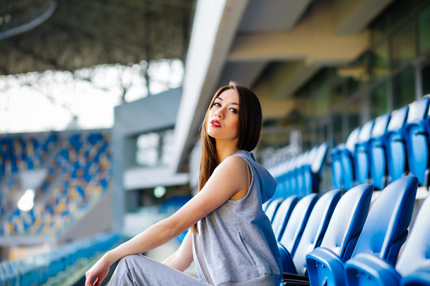Kadeřavý model Evropské mladé brunety vytváří betonové schody na stadionu, nosí potní kalhoty, tenisky - Fotografie, Obrázek