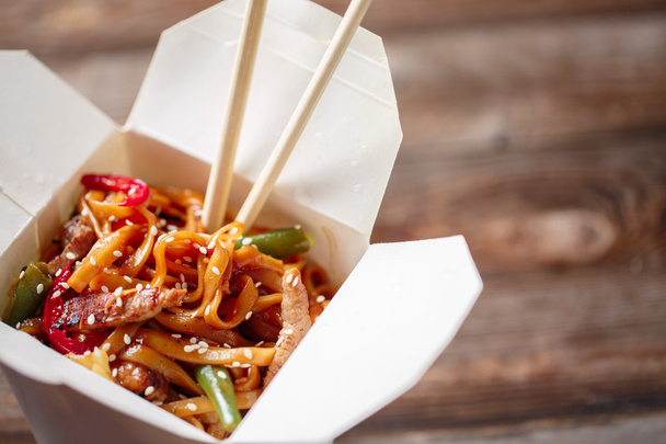 Noodles with pork and vegetables in take-out box on wooden table - Foto, afbeelding