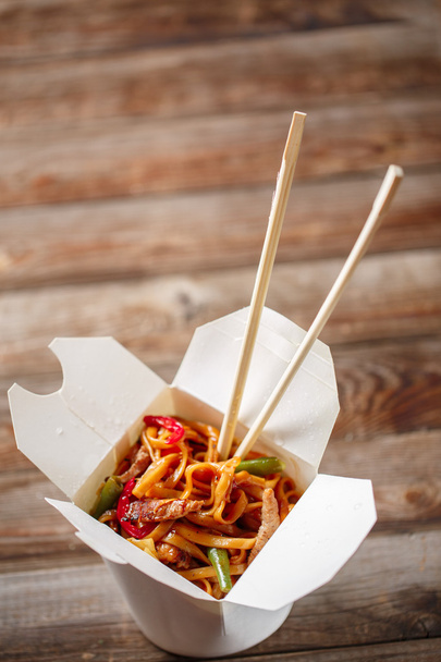 Noodles with pork and vegetables in take-out box on wooden table - Foto, Imagen