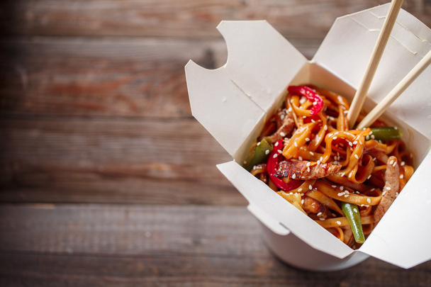 Noodles with pork and vegetables in take-out box on wooden table - Foto, afbeelding