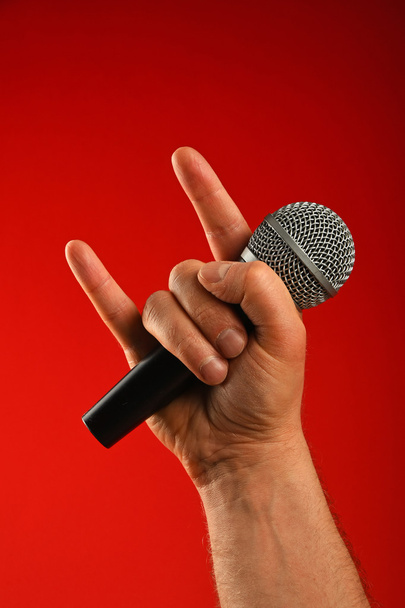 Mano de hombre con micrófono y cuernos de diablo sobre rojo
 - Foto, imagen