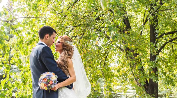 γαμήλιο ζεύγος αγκάλιασμα, η νύφη που κατέχουν ένα μπουκέτο λουλούδια, γαμπρός αγκαλιάζοντάς την - Φωτογραφία, εικόνα